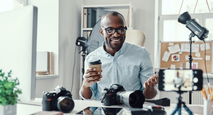 Black influencer surrounded by cameras and technology and holding a coffee