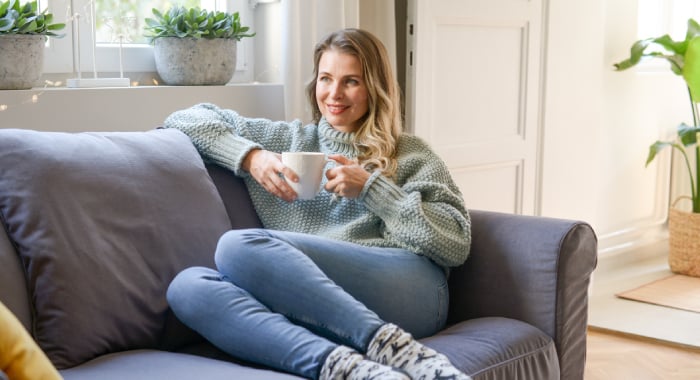 person cozy on their couch in warm clothing and with a hot drink